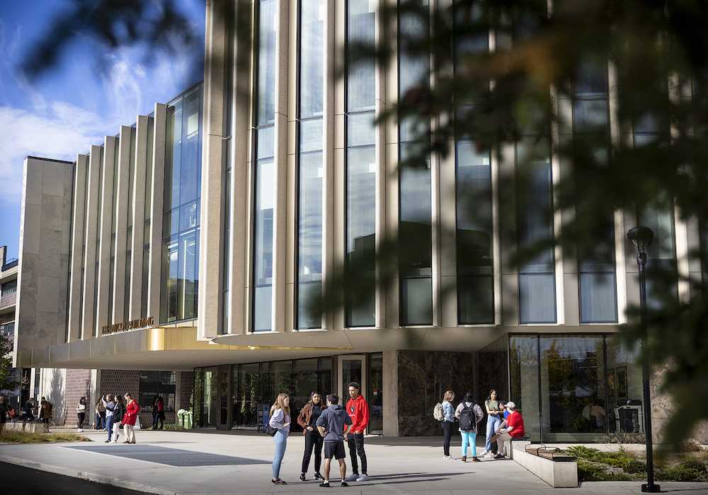 Students in a couple small groups in front of Nicol building, tree branches in foreground
