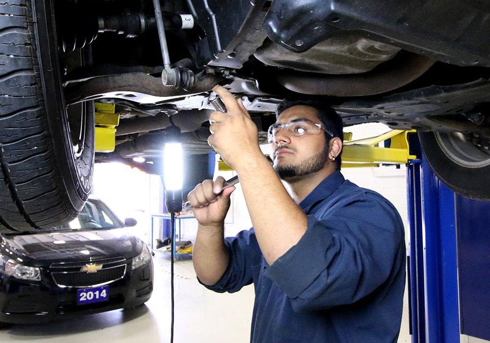 Student in automotive centre working under a vehicle in Sault Colleges automotive centre